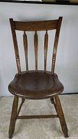 Full front view of the antique wooden arrow back chair showing the backrest with four tapered spindles and solid seat.