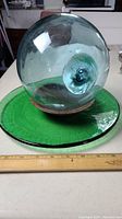 Blue glass ball sitting in wooden dish on green glass dish with ruler showing approximate scale