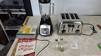 Photo showing Black & Decker blender, Cuisinart toaster, salt and pepper shakers, Betty Crocker parchment paper, and unopened napkins arranged on table.