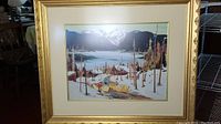 Full view of the framed art print showing the lake, mountains, cabins, and people with canoes.