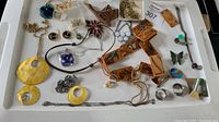 Overview of all the costume jewelry items on a white tray including earrings, necklaces, brooches and pins.