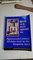 Front cover of the blue softcover book titled 'With Our Past Before Us' focused on 19th-century Kingston architecture, showing a historic building photo.