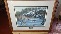 Framed art print titled 'Family Pursuit' by Paul Rankin showing wolves in a snowy forest, displayed in a wooden frame with matting.