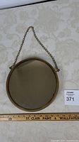 Top view of the 10-inch round mirror with hanging chain showing the mirror surface and chain on patterned surface.