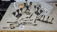 Overview of all items in the lot on table including multiple cutlery pieces, tarnish remover, candle snuffer, candles and silver candelabrum.