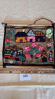 Full view of large 36x34 inch Mexican village textile wall hanging showing colorful embroidered houses, trees, and flowers on burlap fabric