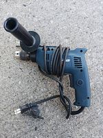 Right side view of the blue Mastercraft hammer drill showing the wire cord wrapped, the keyed chuck, side handle, and power cord with plug.