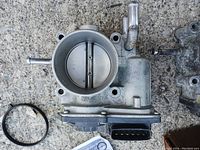 Top view of one throttle body showing circular air passage and butterfly valve inside, attached electrical connector and hose fittings.