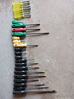 Overview of all 3 screwdriver sets arranged on the floor: yellow bolt screwdrivers, colored smaller screwdrivers, and black-handled screwdrivers.