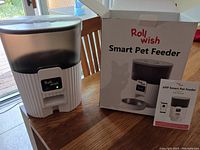 Rollwish Smart Pet Feeder out of the box with digital display on unit, alongside its original box and user manual.