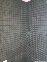 Corner wall installation showing black acoustic foam panels with pyramid texture for sound insulation.