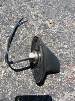 Top view of black shark fin radio antenna showing threaded mounting stud and attached cable on asphalt background.