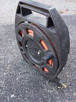 Side view of black NOMA extension cord reel showing orange cord through holes and integrated handle