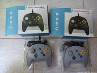 Two Classic Controllers in original blue and white boxes, and both controllers unboxed in plastic trays showing gray color with multicolored buttons.