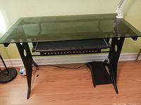 Full view of the glass desk showing the glass surface, keyboard tray, and metal frame with computer tower platform.