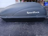 Side view of black SportRack cargo box showing logo and two locking latches