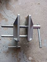 Top and side view of the L-shaped metal corner bench vise showing vice jaws, central clamping screw, and mounting screws.