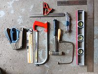 Photo showing assorted hand tools including staple gun, hacksaws, hammer, speed square, spirit level, hex keys, and screwdriver.