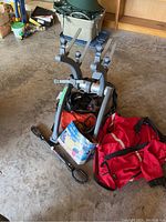 Photo showing Saris bike rack with adjustable arms, two helmets underneath, and a red jacket spread in front along with air compressor components.