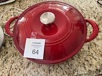 Top view of red enameled cast iron covered oval Dutch oven with metal lid knob and two side handles.