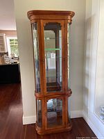 Full view of the tall curio cabinet made of wood and glass with curved edges and two main compartments.