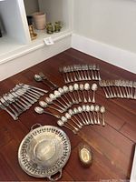 Assorted stainless steel flatware and two silver plated bowls arranged on wood floor