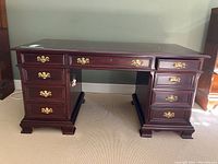 Front view of solid mahogany 7-drawer desk with brass handles on carpeted floor.