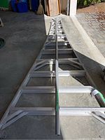 Full view of aluminum fruit ladder frame with extension pole laid flat in garage