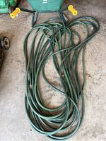 Top view of several long green garden hoses laid in front of the wheelbarrow