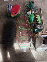 Overview of tomato cages, garden netting, watering can, and assorted gardening tools arranged in garage on floor.