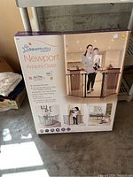 Front view of new Dreambaby Newport Adapta-Gate box showing gate installed in home setting with woman and child, product features noted.