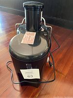 Front view of Omega electric juicer showing stainless steel body, black pulp container, and electric cord wrapped around it.