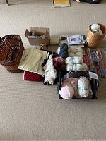 Wide view of the entire assortment spread on carpet including yarn, baskets, knitting magazines, and needles.