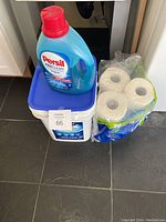 Persil ProClean liquid detergent bottle, Kirkland powder detergent container and paper towel rolls