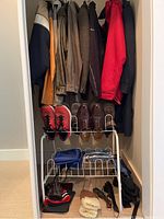 Wide shot showing hanging men's jackets in various colors including navy, beige, grey, brown, and dark colors. Shoe rack beneath holds multiple pairs of men’s shoes in sizes US 9.5 and above.