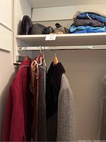 View of closet space with hanging coats, ties, and folded men's clothing items on shelf including hats and t-shirts.