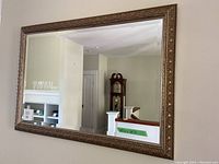 Full view of large wall mirror reflecting room interior, showing ornate bronze/gold frame.