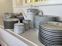 Full view of Noritake Blue Hill china with stacked plates, coffee pot, creamer, sugar bowl, cups and pepper shaker showing extensive set.