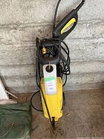 Full view of the yellow and black Karcher pressure washer unit with cable and attached hose, trigger gun visible on top, showing its used condition and dust.