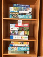 Shelf with stacked jigsaw puzzle boxes of varying brands and piece counts, colors, and themes.