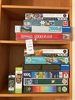 Photo of puzzle boxes stacked on shelves showing various brands and piece counts including Eurographics, Ravensburger, Waddingtons, Jumbo, Schmidt, Cobble Hill, Buffalo.
