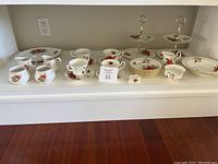 Full set of Royal Albert Poinsettia china pieces displayed together on a shelf, including cups, plates, and serving trays.