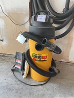 Shop-Vac Hang Up 18 gallon vacuum with attached hoses, power cord, and filter bags on floor.