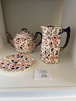 Full view of the tea pot, chocolate pot, and matching plate with floral decoration in red, blue, and gold tones.