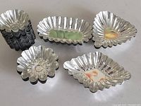 Photo of assorted stack and individual vintage metal molds showing various shelled and fluted shapes in shiny silver metal.