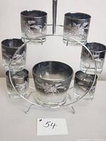 Front view of 6 smoked silver glasses and matching ice bucket on the Ferris wheel metal carrier showing floral etched design.