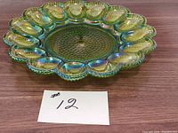 Top angled view of green hobnail carnival glass egg plate showing 12 egg-shaped compartments and hobnail texture on a wooden table.