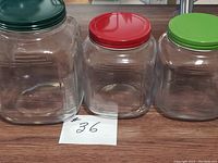 Set of three clear glass jars with colored screw-on lids placed side by side on a wooden surface showing size variation