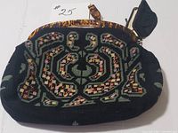 Front view of vintage needlepoint handbag with detailed floral and geometric needlework, depicting colors including green, pink, yellow on black background. Acrylic tortoiseshell-style handles and frame visible. Attached small coin purse with black fabric is shown hanging from the frame.
