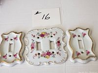 Set of three ceramic hand-painted outlet covers arranged on white background showing floral patterns and gold edging.